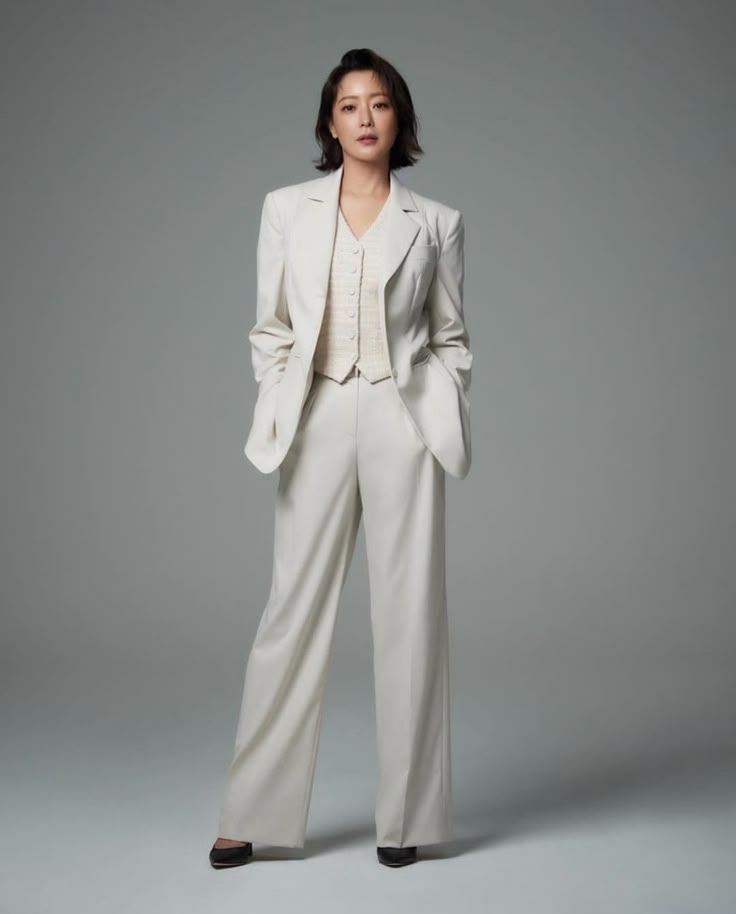 a woman in a white suit and black shoes poses for the camera with her hands on her hips