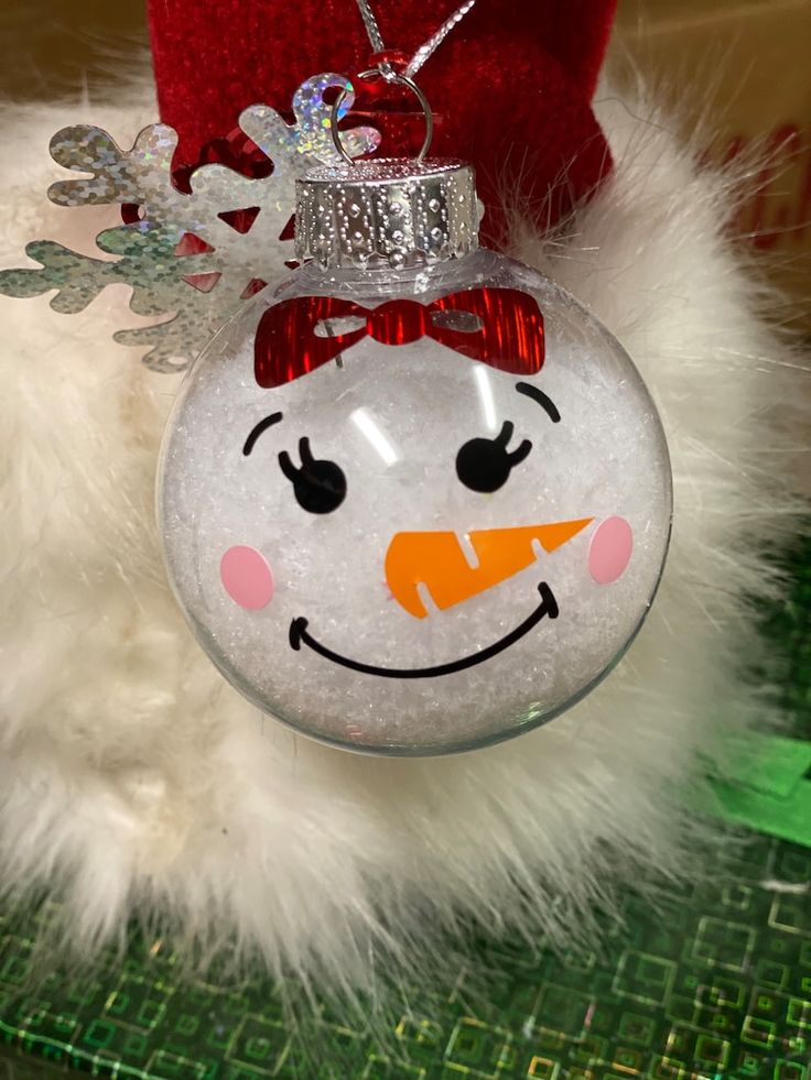 a glass ornament with a snowman face on it's head, hanging from a christmas tree