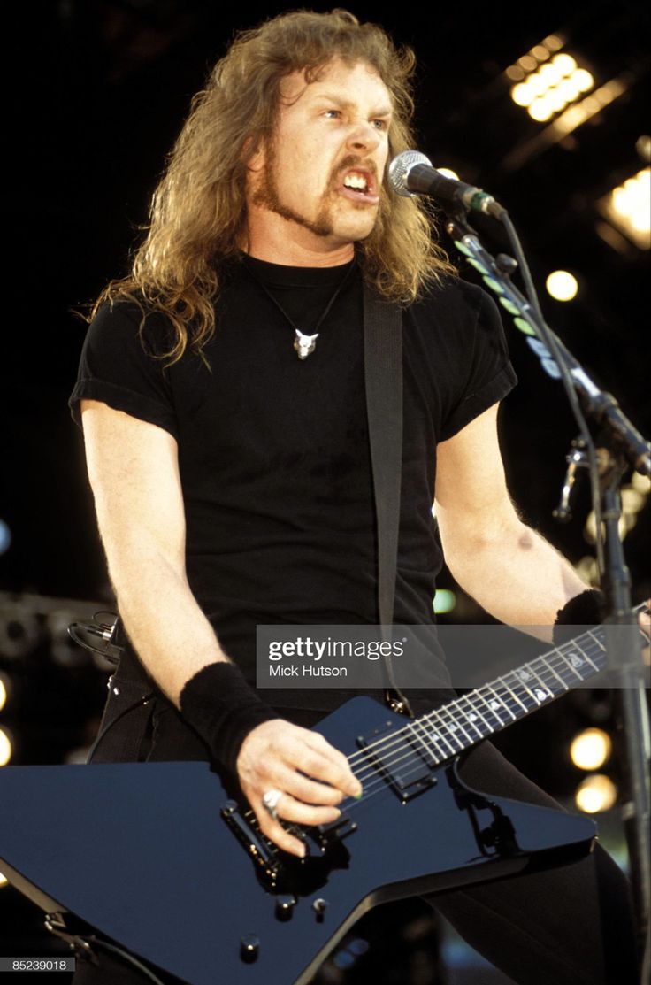 a man with long hair playing an electric guitar in front of a microphone on stage