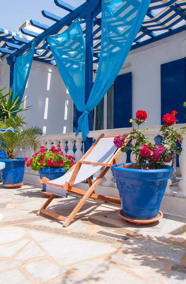 a deck chair and flower pots on a patio with blue curtains over the sun room