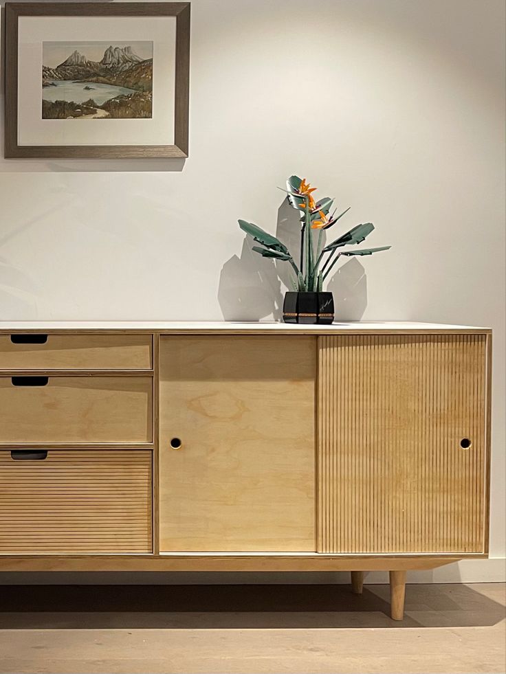 a vase with flowers on top of a wooden cabinet next to a painting and framed pictures