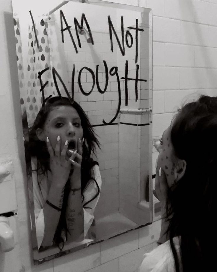 a woman brushing her teeth in front of a bathroom mirror with graffiti on the wall