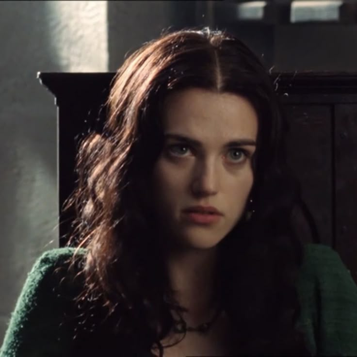 a woman with long brown hair sitting in front of a wooden cabinet and looking at the camera