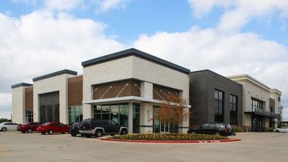 an empty parking lot in front of a building with cars parked on the street outside