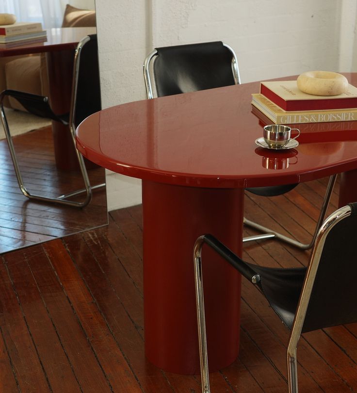 a red table with two black chairs next to it and a stack of books on top