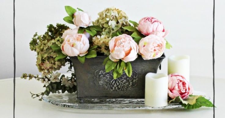 flowers and candles sit on a table in front of a white wall with black frame