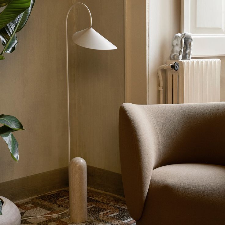 a living room with a chair, lamp and potted plant on the floor next to a radiator