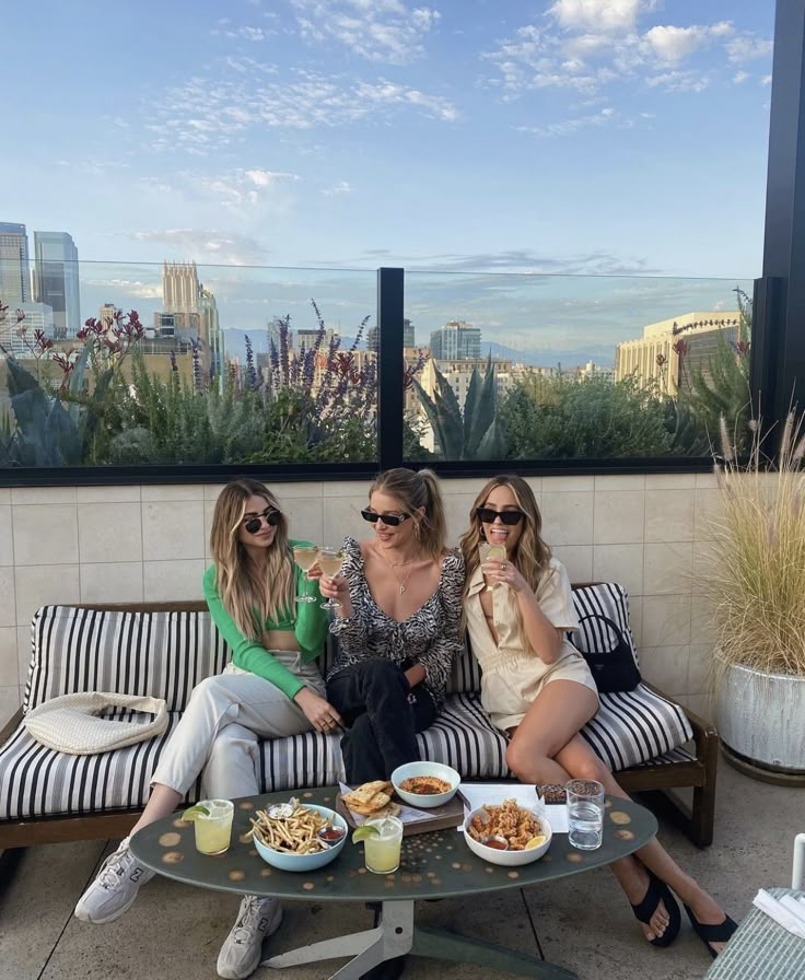 two women sitting on a bench with food and drinks in front of the city skyline