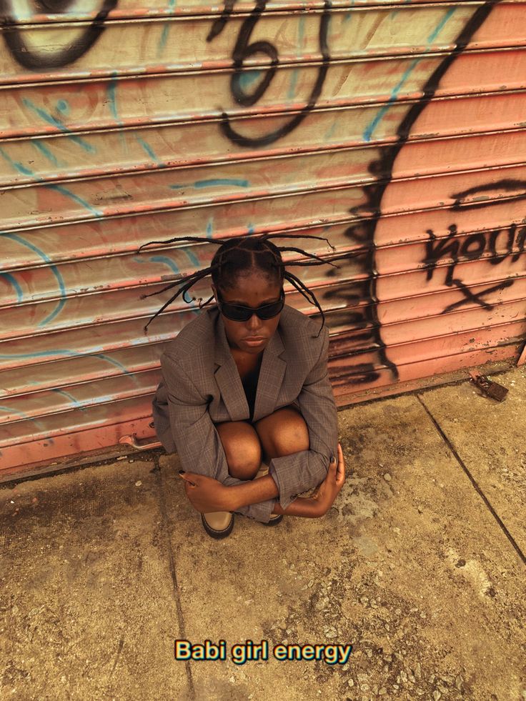 a man sitting on the ground in front of a wall with graffiti written on it