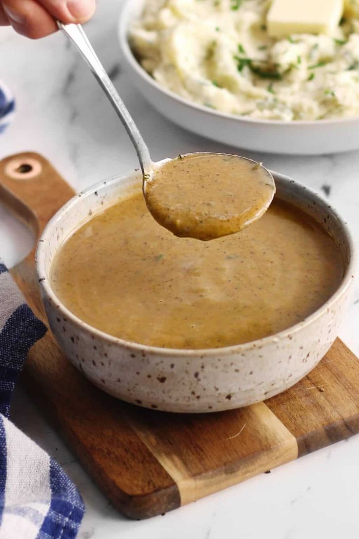 a person spooning mashed potatoes out of a bowl with gravy on the side