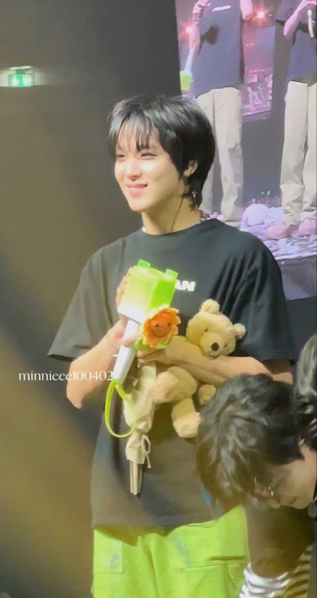 a young man holding a teddy bear while standing next to a little boy in front of him