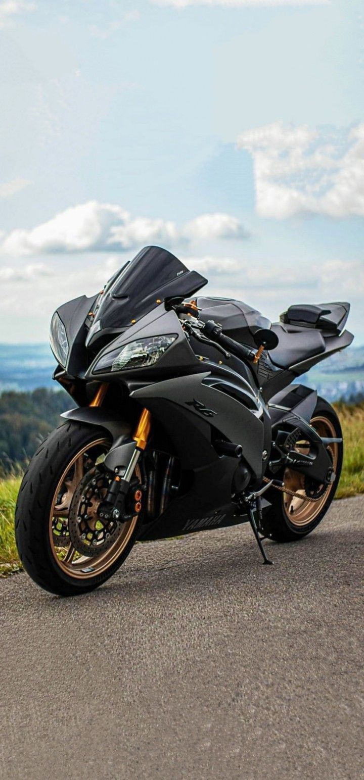 a black motorcycle parked on the side of a road next to a lush green hillside