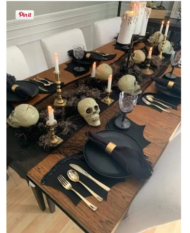 the table is set with black and gold plates, silverware, candles and skulls