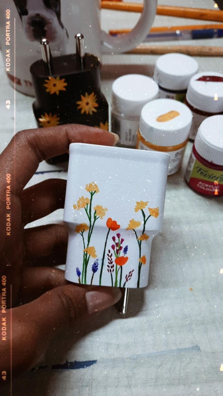 a person is holding a small piece of glass with flowers painted on it and other crafting supplies in the background