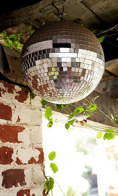 a disco ball hanging from the ceiling next to a brick wall with ivy growing on it