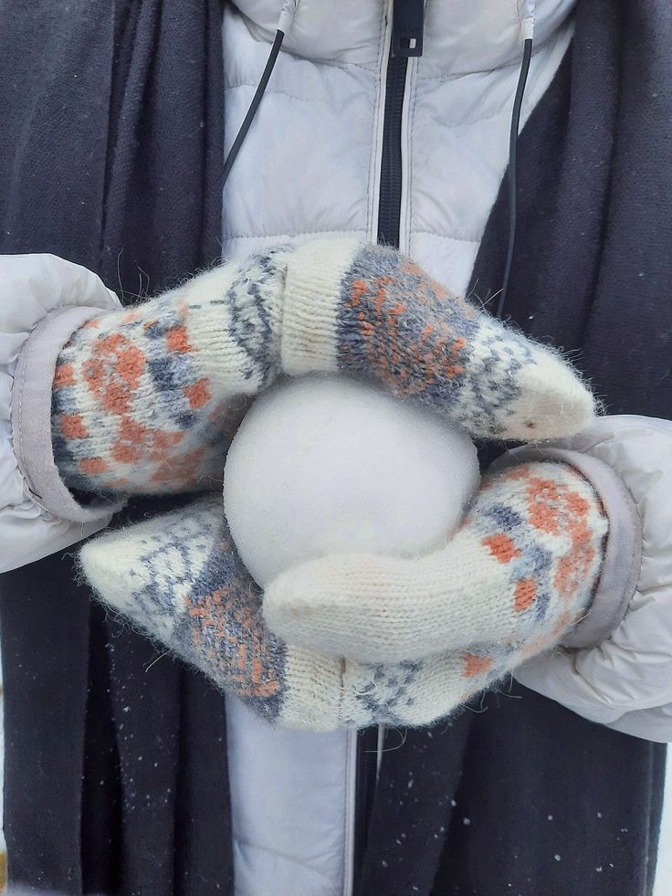 a person holding a snowball in their hands and wearing mittens on the other hand