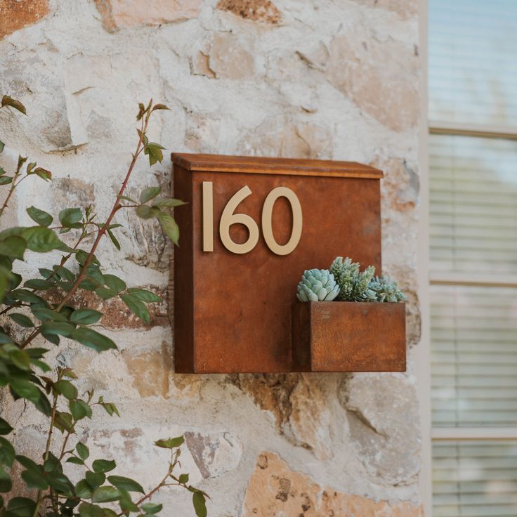 a house number sign mounted to the side of a stone wall with succulents