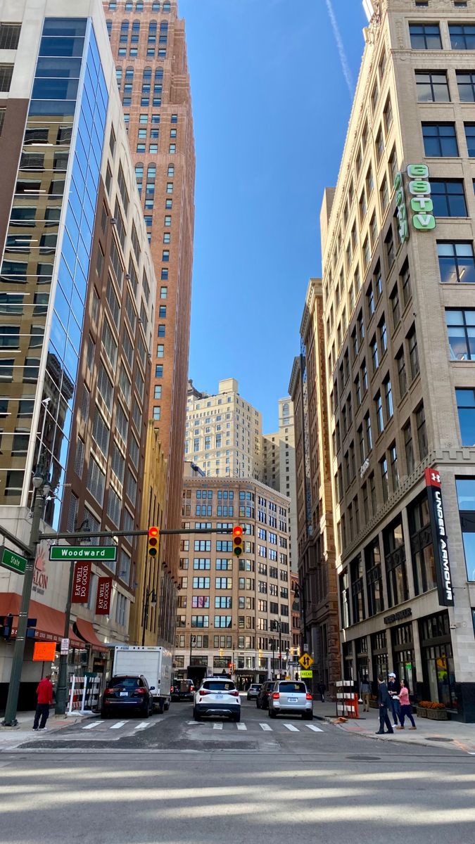 an intersection with cars and people walking on the sidewalk in front of tall buildings,