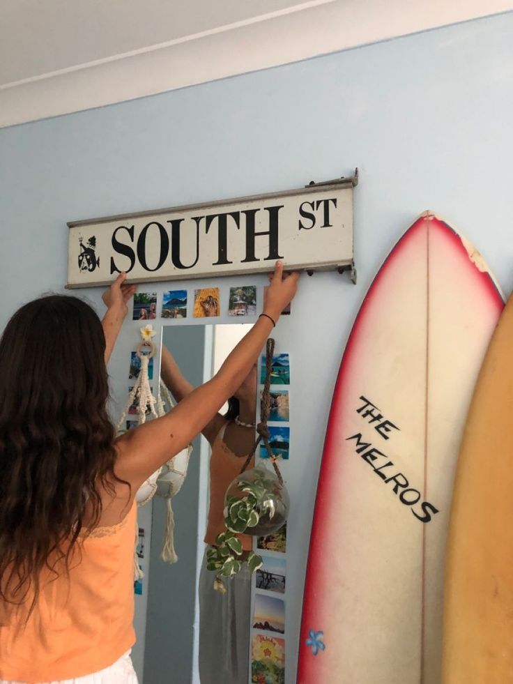 a woman holding up a sign that says south st in front of two surfboards