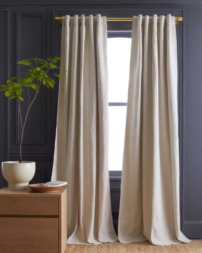 a white curtain hanging on the side of a window next to a potted plant