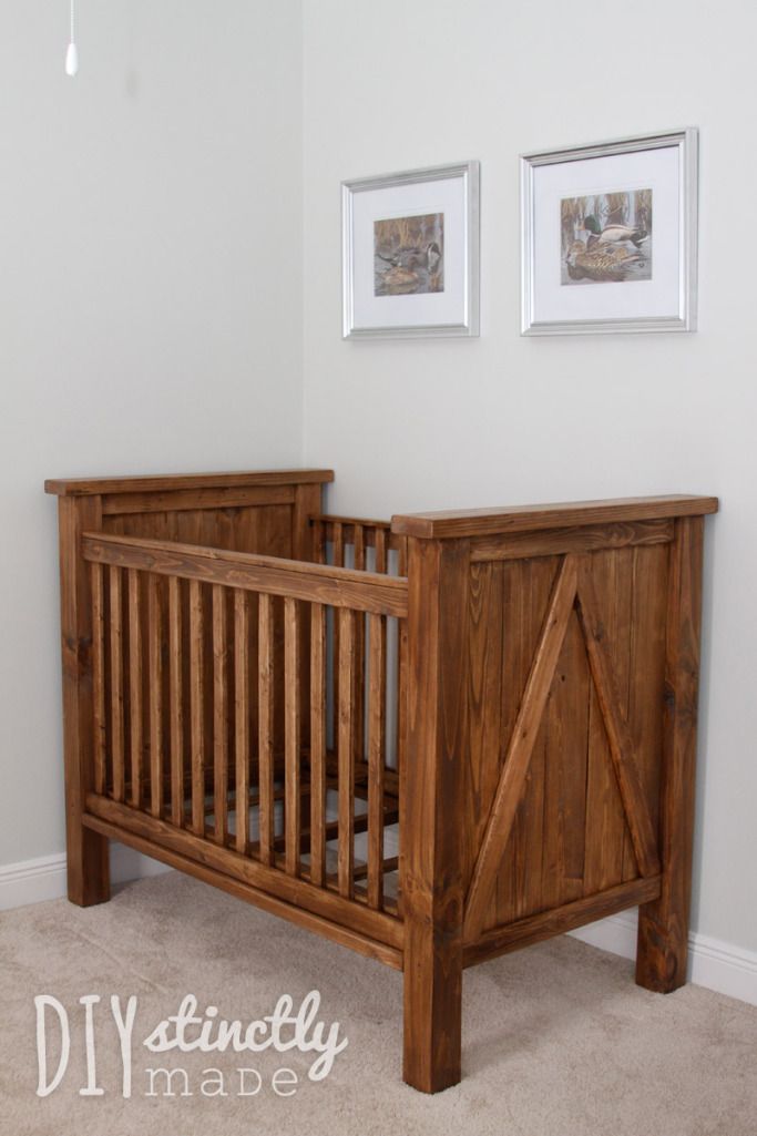 a wooden crib in the corner of a room with pictures on the wall above it