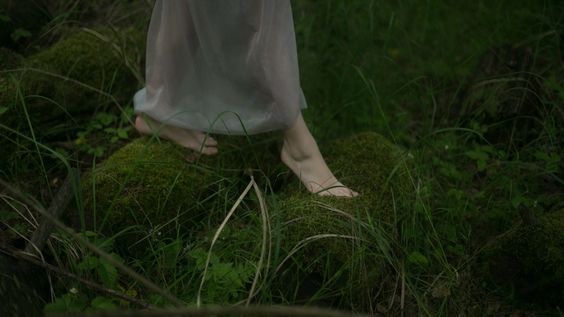 a woman's legs in white dress standing on mossy ground next to trees