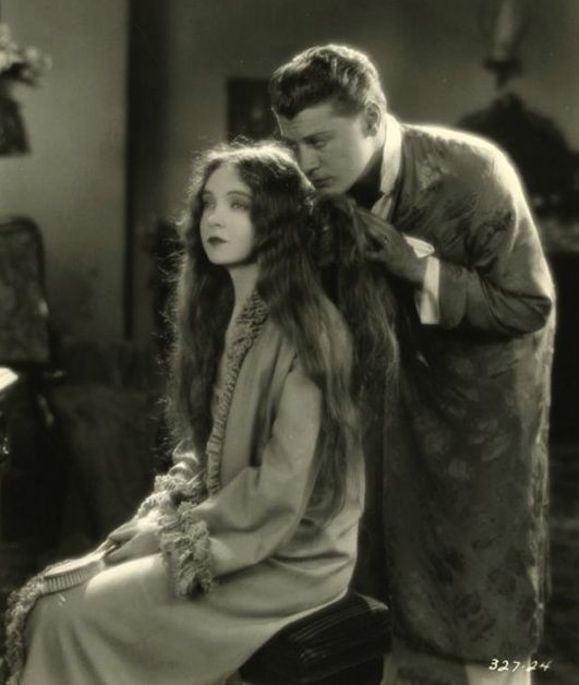 an old black and white photo of a man combing a woman's hair