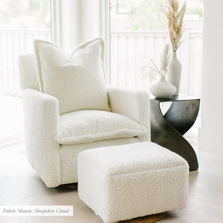 a white chair and footstool in front of a window with a vase on it