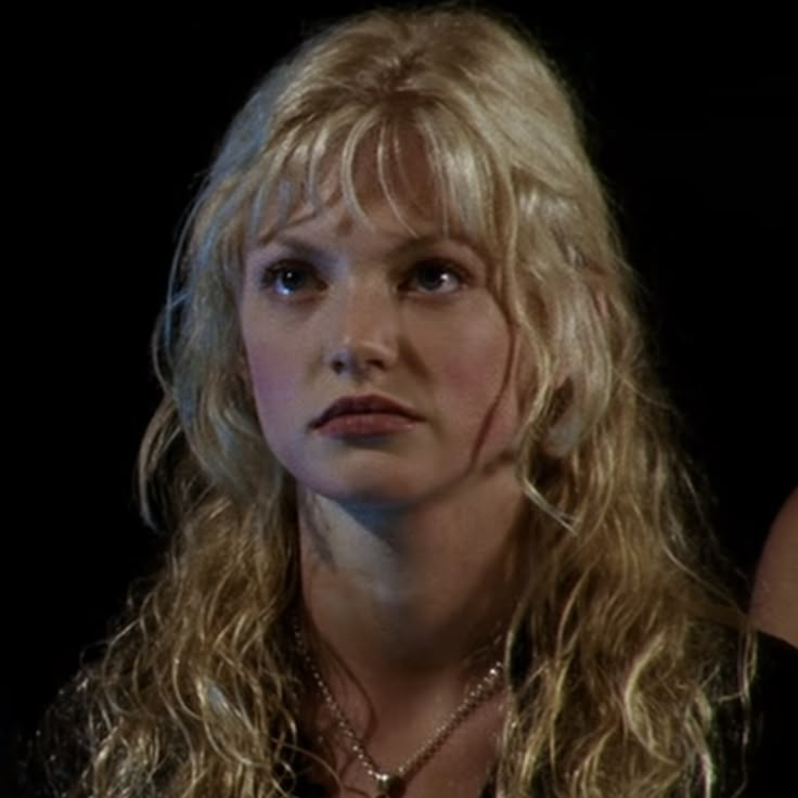 a woman with long blonde hair wearing a black shirt and necklace looking off to the side