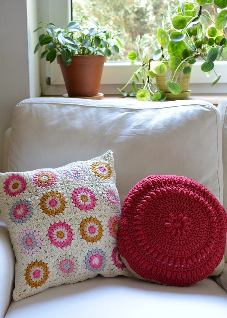 a crocheted pillow sits on a white couch next to a potted plant