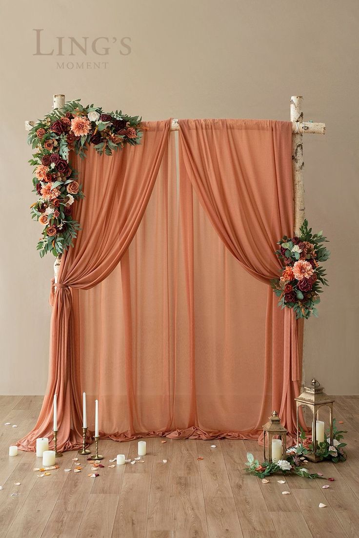 an orange curtain with flowers and candles in front of it on a wooden floor next to a cross