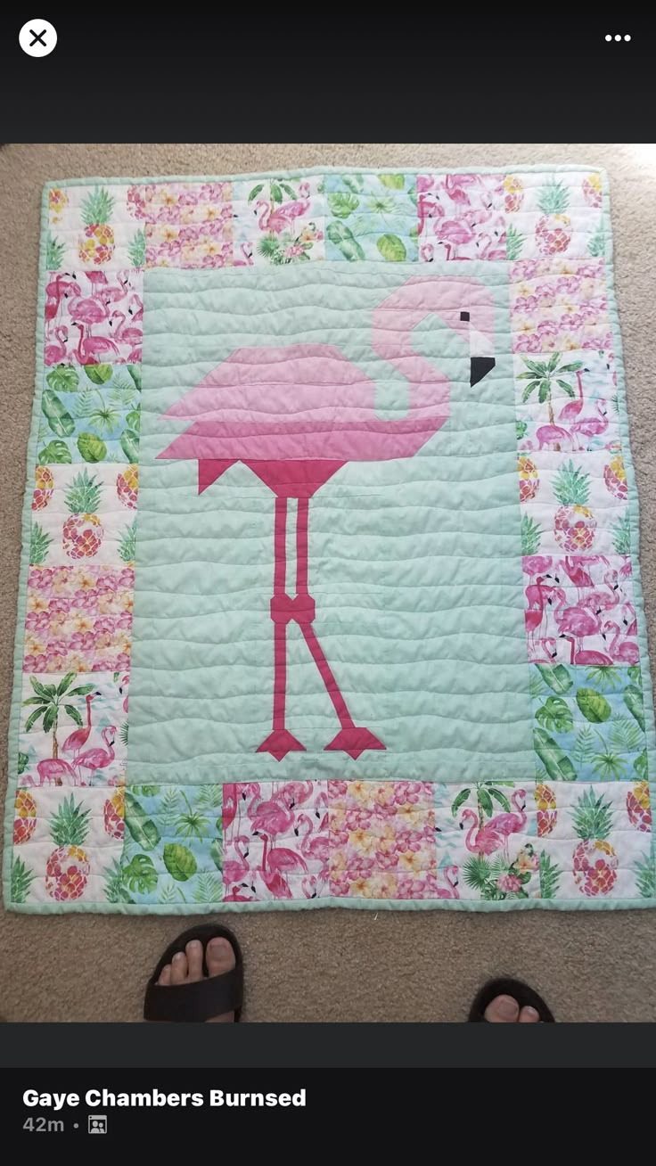 a pink flamingo quilted on the floor next to someone's feet and sandals