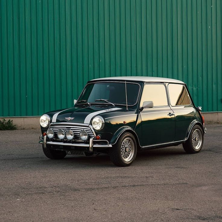 an old mini car parked in front of a green building with a red door and window