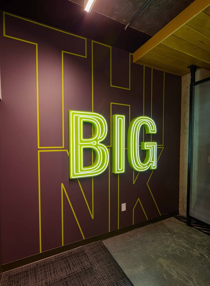 a big neon sign on the side of a wall next to a glass door in an office