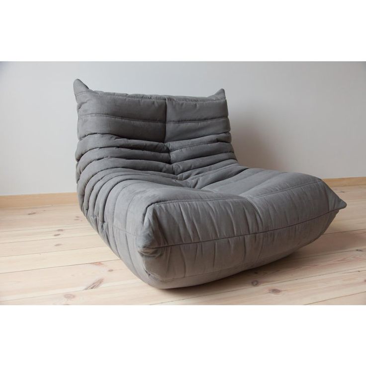 a large gray chair sitting on top of a wooden floor next to a white wall