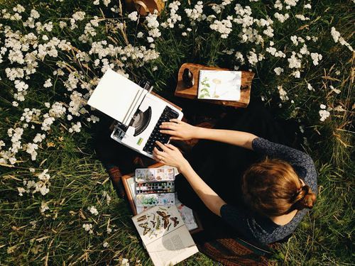 a woman sitting in the grass with her laptop and books on top of her lap