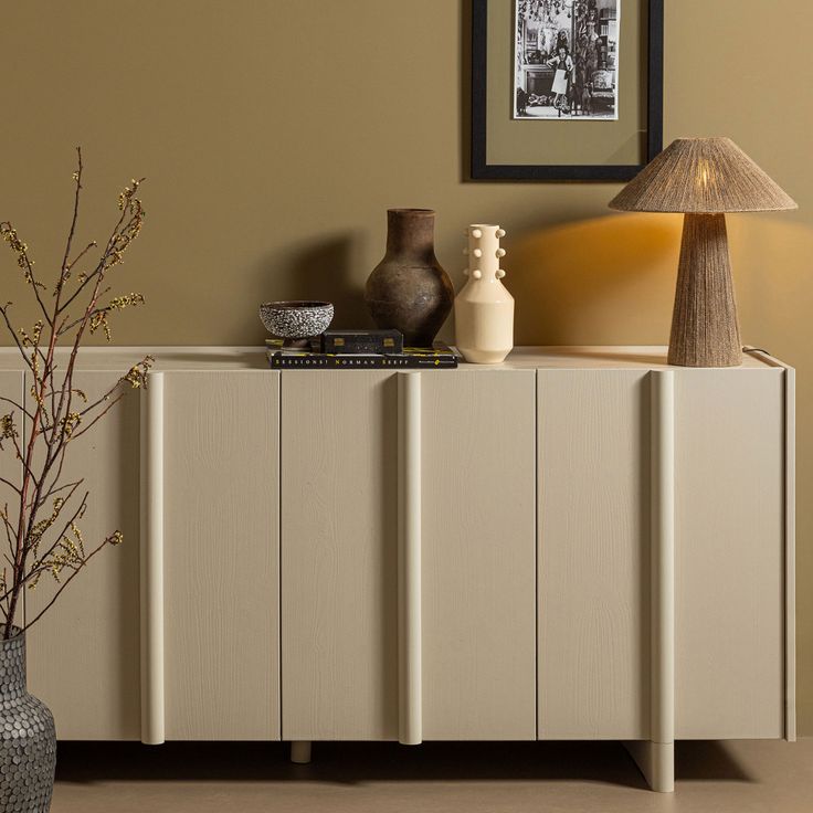 a sideboard with two vases on it and a lamp in the corner next to it