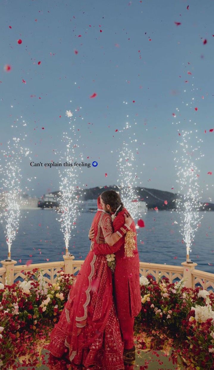 two people standing in front of flowers and water with confetti falling from the sky