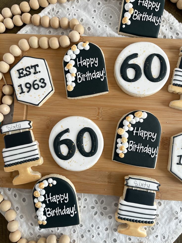 decorated birthday cookies with black and white frosting are arranged on a wooden cutting board