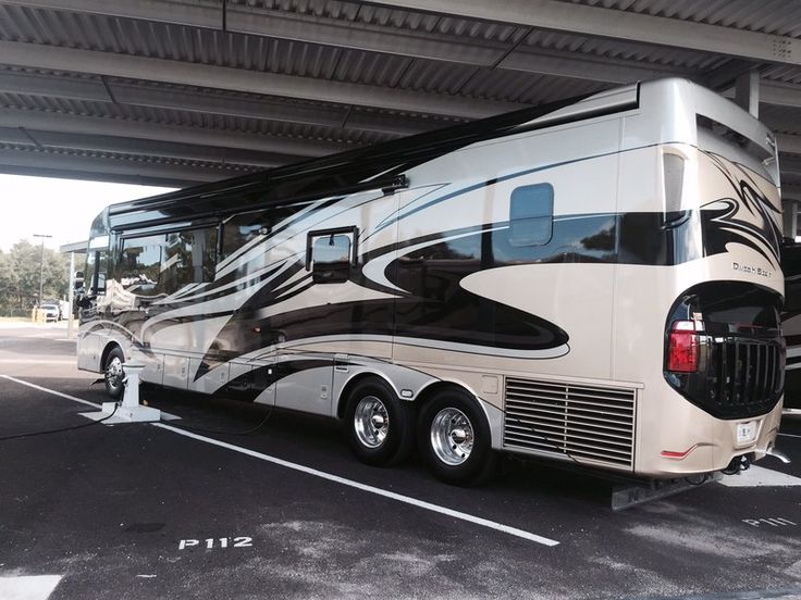 a motor home parked in a parking lot next to another vehicle under a roof structure