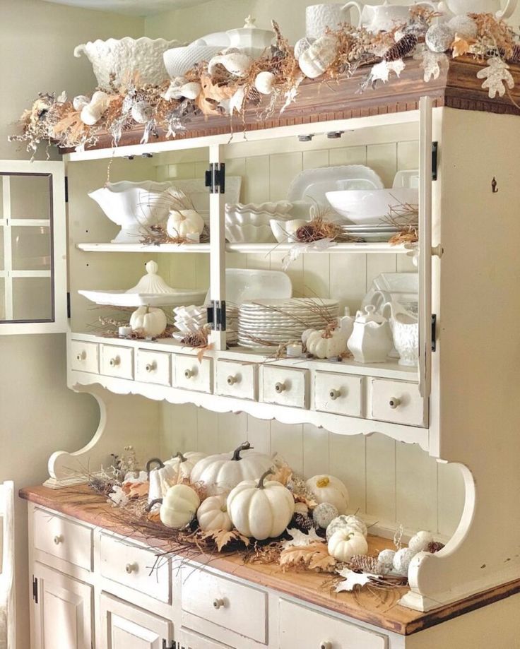 a white hutch filled with lots of dishes and pumpkins on top of it