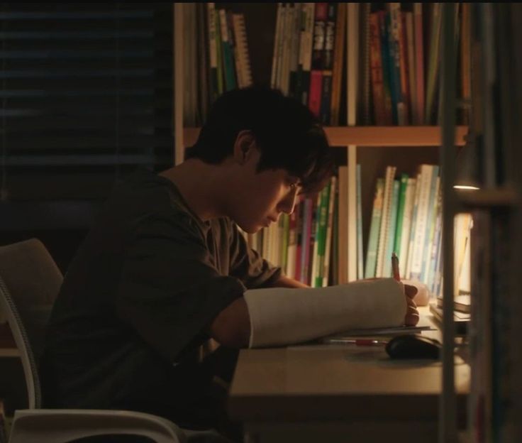 a young man sitting at a desk in front of a book shelf with books on it