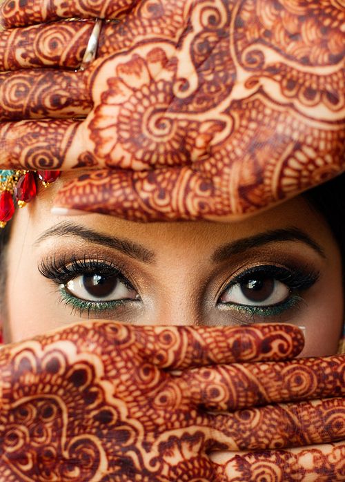 a close up of a woman's face with her hands on her head and eyes covered in henna