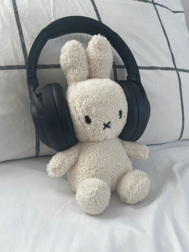 a white stuffed animal with headphones on it's ears sitting on a bed