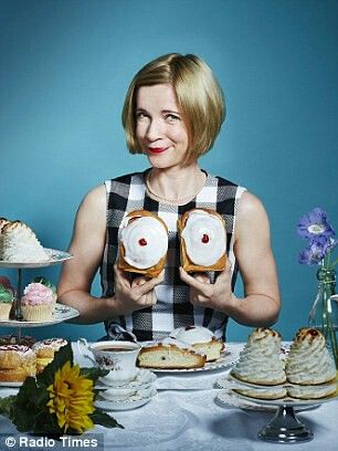 a woman sitting at a table holding two donuts in front of her face, with other desserts on the table behind her