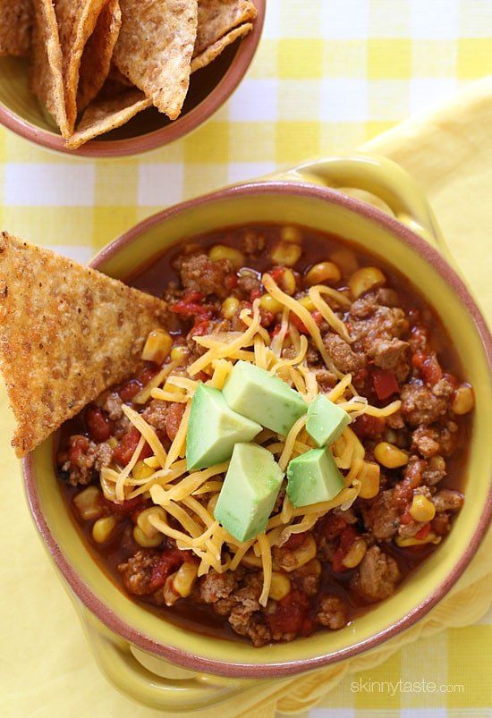 two bowls filled with chili, beans and tortilla chips on top of a yellow checkered table cloth