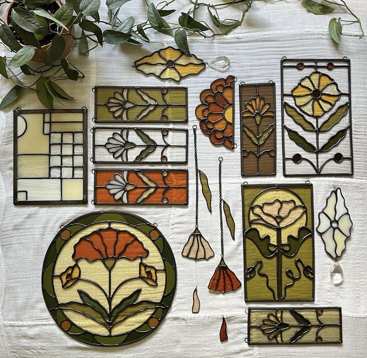 several stained glass pieces are arranged on a white tablecloth with green leaves and flowers