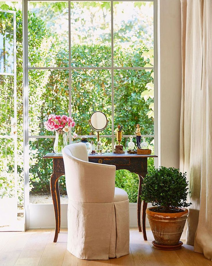 a white chair sitting in front of a window next to a potted plant on top of a wooden table