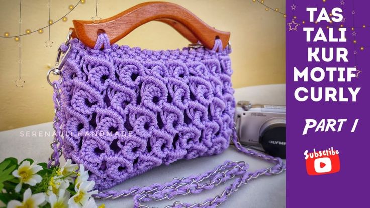 a purple crochet purse sitting on top of a table next to a flower