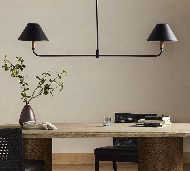 a dining room table with two black lamps hanging from it's sides and a vase on the other side